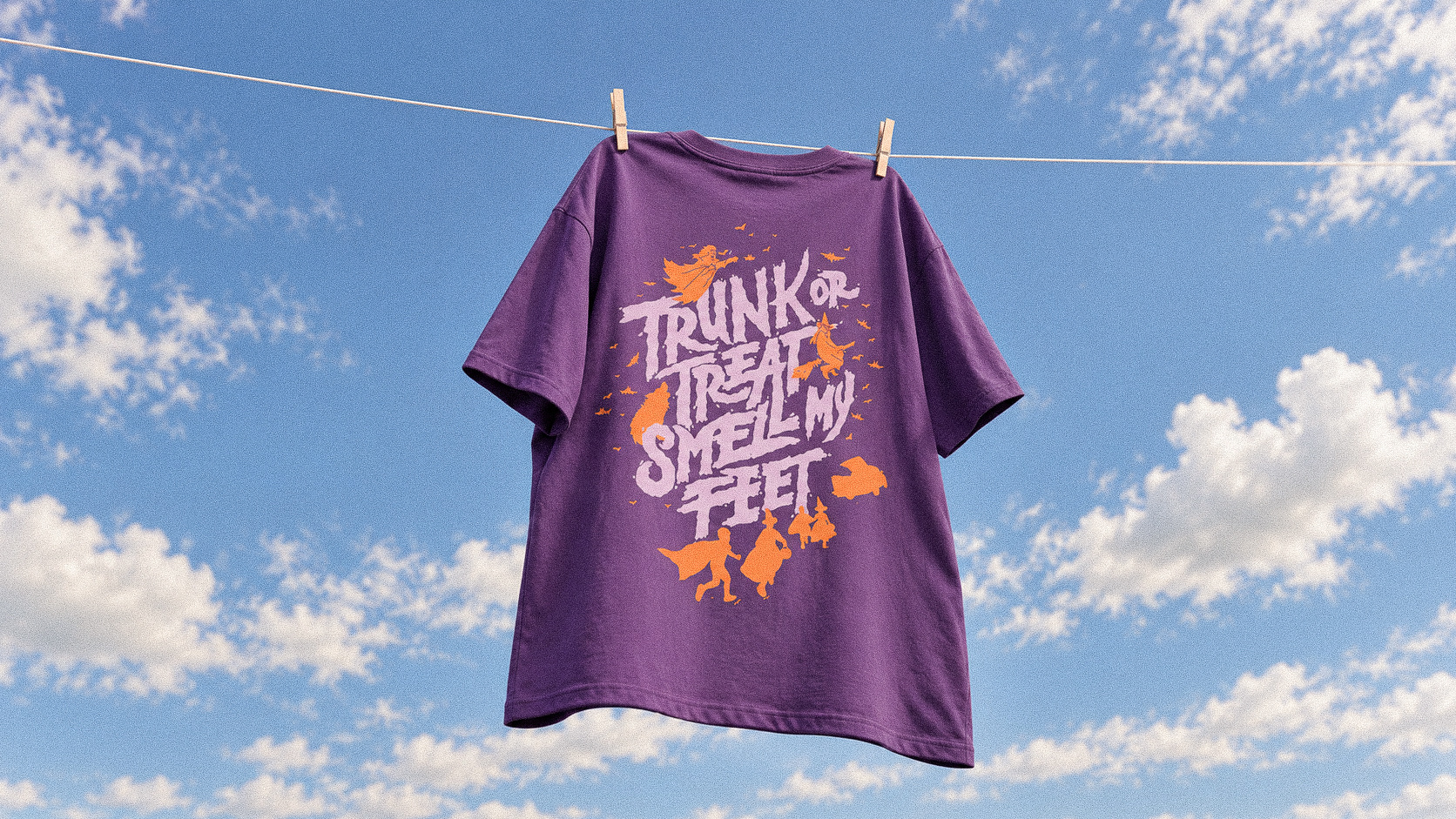 Purple illustrated fundraiser tee hanging on a clothesline against a blue sky